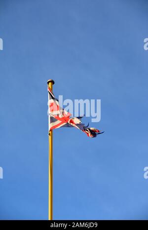 Una bandiera Union Jack infranta e tenuta contro un cielo blu chiaro Foto Stock