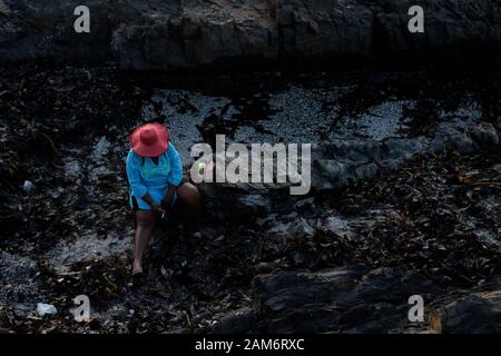 Una donna in un cappello fuma una sigaretta su una spiaggia in Cape Town Atlantic Seaboard sobborgo di Seapoint in Sud Africa Foto Stock