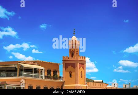 Vista della torre più grande sulla piazza principale della città di Jemaa EL Fnaa. E' una bella giornata di sole al mercato nella medina di Marrakech Foto Stock