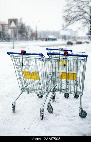 Carrello vuoto in piedi sulla strada in inverno. Il carro del mercato, il supermercato e il parcheggio. Foto Stock