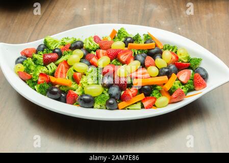 Primo piano di Macedonia di frutta con broccoli, uva verde e nera, fettine o cubetti di fragole e carote. Pasto delizioso, nutriente e sano in un pasto Foto Stock