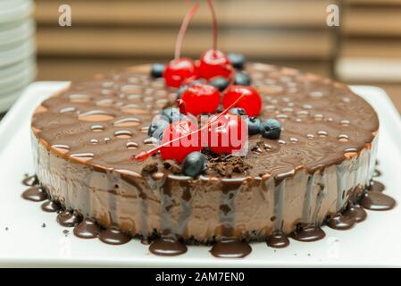 Bellissimo e gustoso dessert al cioccolato, con sciroppo e condimento di ciliegia e mirtillo. Deliziosa torta al cioccolato su piatto bianco. Cucina gourmet concetto. Se Foto Stock