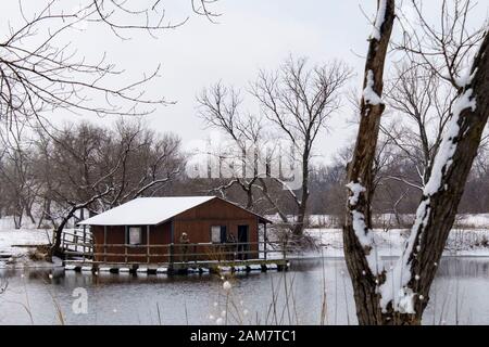 Due uomini pesce fuori da un galleggiante dock di pesca in un stagno dopo una nevicata invernale. Stati Uniti d'America. Foto Stock