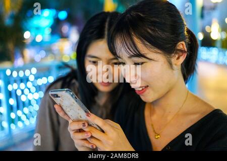 Zhuhai, Cina, Novembre 2018. Le ragazze asiatiche giovani stanno guardando qualcosa di divertente nel telefono cellulare. Foto Stock