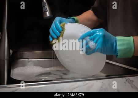 Piatti per il lavaggio delle mani di un modello con guanti in gomma blu chiaro con polsini anti-gocciolamento. Foto Stock