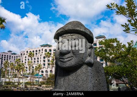 Jeju, Corea, 6th, Marzo 2019. DOL Hareubang con Lotte Hotel Jeju sullo sfondo. DOL Hareubang sono statue di pietra che si possono trovare in tutto intorno a Jej Foto Stock