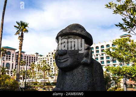 Jeju, Corea, 10th, Marzo 2019. DOL Hareubang con Lotte Hotel Jeju sullo sfondo. Sono statue di pietra che si possono trovare in tutta l'isola di Jeju Foto Stock