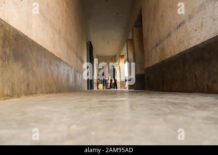 Vista ad angolo basso delle persone in piedi alla fine del lungo corridoio nell'edificio vecchio con pavimento vuoto in primo piano Foto Stock