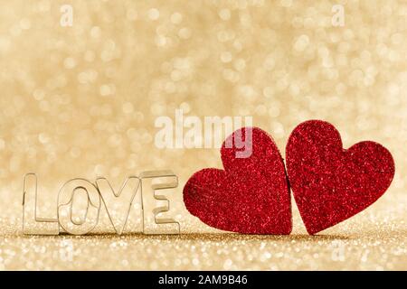 Due fatti a mano rosso glitter cuori e la parola amore su golden luminose luci glitter sfondo bokeh di fondo Foto Stock