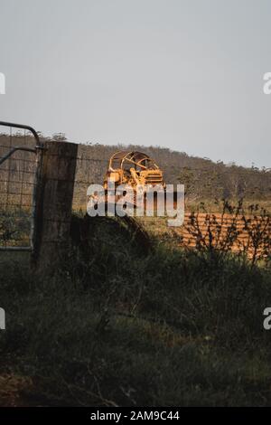 Macchina movimento terra e attrezzatura agricola seduto in un campo dietro una recinzione su una proprietà vicino Comboyne, Nuovo Galles del Sud. Foto Stock