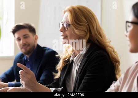 Mentore di mezza età che parla con i giovani alla riunione di gruppo Foto Stock