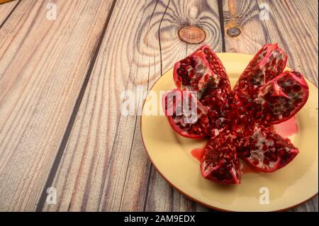 Mature succosa melagrana tagliata in più pezzi su una piastra di ceramica su uno sfondo di legno. Close up Foto Stock