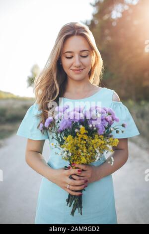 Una bella ragazza è in piedi con un bouquet nelle sue mani. Il sole sta rompendo attraverso la sua spalla. Foto Stock