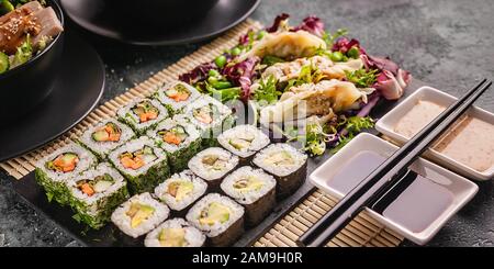 Banner cibo asiatico. Chiudete i rotoli di sushi con verdure e gnocchi. Cucina cinese su sfondo grigio cemento Foto Stock