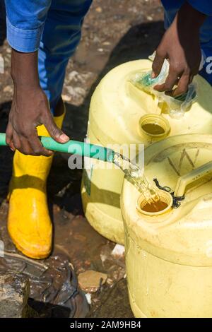 Un giovane uomo e alcuni ragazzi locali riempiono i contenitori d'acqua da un tubo d'acqua dolce, Korogocho slum, Nairobi, Kenya Foto Stock