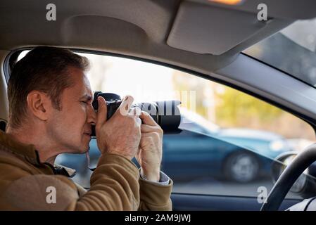 Giovane uomo con una fotocamera dslr in un'auto. Foto Stock