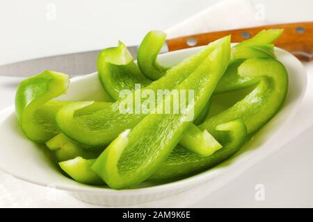 Affettare il peperone verde in una ciotola bianca e un coltello da cucina accanto Foto Stock