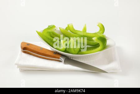 Affettare il peperone verde in una ciotola bianca e un coltello da cucina accanto Foto Stock