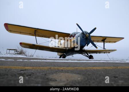 Una foto dal campo di aviazione durante l'inverno. Il vecchio biplano è fermo sulla pista e in attesa che il tempo migliori in modo che sia in grado di volare nuovamente. Foto Stock