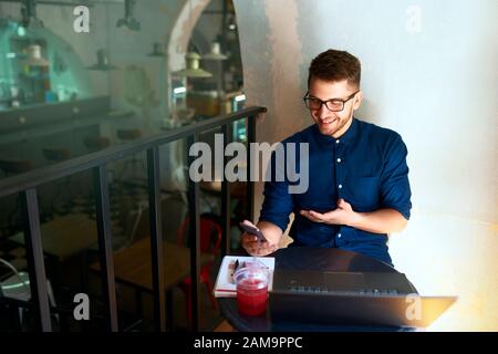 Freelancer sorridente con telelavoro tramite video chat online. Distratto dall'uomo d'affari che tiene il telefono mobile. Uomo in occhiali con Foto Stock