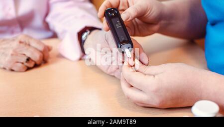 Infermiere amministra il test del diabete a senior in casa di cura Foto Stock