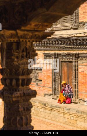 Donna nepalese anziana sui gradini di un tempio a Bhaktapur, Nepal Foto Stock