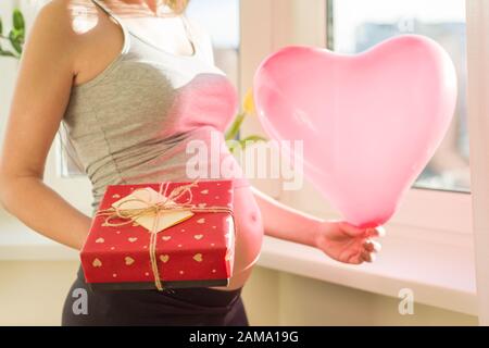 Donna incinta con confezione regalo e palloncino cuore Foto Stock