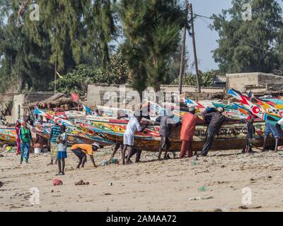 Nianing, Senegal - Gennaio 2, 2019: i pescatori la raccolta di pesce di legno colorato barca fisher permanente sulla spiaggia. Africa Foto Stock