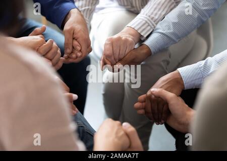 Persone sedute in cerchio che tengono le mani durante la sessione di terapia di gruppo Foto Stock