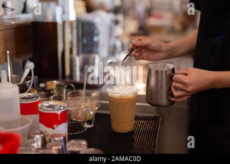 Il barista ha montato a mano il panna da montare sulla parte superiore del caffè ghiacciato. Foto Stock