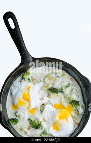 Frittata di broccoli con uova in camicia in una padella su fondo bianco. Foto Stock