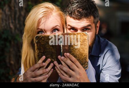 Concetto di storia scioccante. Coppia in amore leggere libro antico, sfondo scuro. Facce stupiti di coppia nascosto da vecchio libro disordinato. L'uomo e la donna hanno trovato informazioni scioccanti nel vecchio notebook. Foto Stock