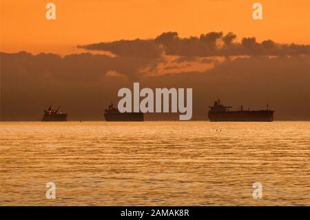 Le navi in attesa al di ancoraggio nel Golfo del Messico presso sunrise, prima di entrare in Galveston Bay sul loro modo al Porto di Houston, Texas, Stati Uniti d'America Foto Stock