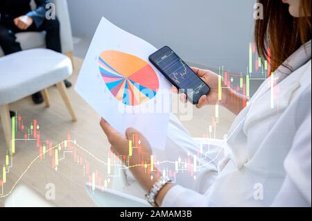 Le donne di affari che indossano vestiti bianchi sono felici di giocare i telefoni mobili, controlli il grafico superiore di crescita del commercio Foto Stock