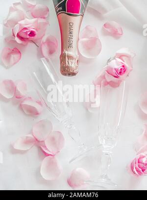 Bicchieri da champagne in cristallo per matrimoni su un tovagliolo in raso con una bottiglia di champagne e petali di rosa Foto Stock