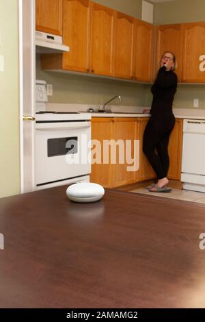 donna sullo sfondo della cucina che chiama il suo smart home mini altoparlante Foto Stock