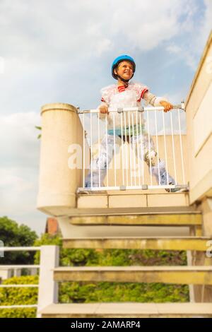 Il ragazzo si trova vicino alla porta di sicurezza dei bambini, alle scale nella pellicola a bolle d'aria e al casco dalla madre sovraprotettiva Foto Stock