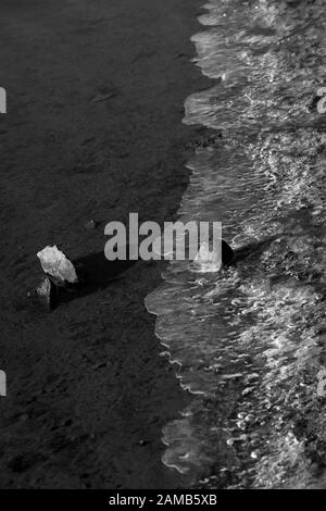 Un'immagine ravvicinata minimalista di pietre, acqua e ghiaccio catturati da un lago in un momento Foto Stock