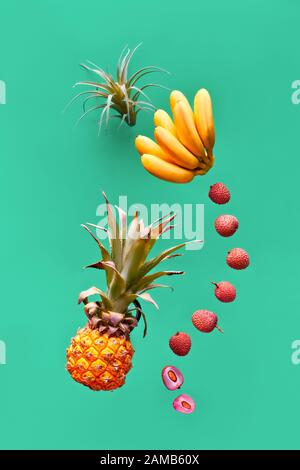 Assortimento di frutta tropicale, levitazione su sfondo verde. Ananas, lichee e banana - frutti esotici di colore giallo, arancione e rosso. Foto Stock