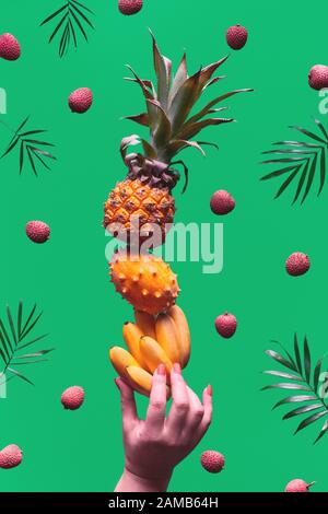 Assortimento di frutti tropicali, piramide che bilancia o mano umana su sfondo verde. Ananas, kiwano, kiwi, lichee e banana - torre fatta di esotico Foto Stock