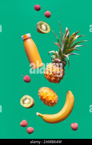 Assortimento di frutta tropicale e bottiglia di frullato arancione su sfondo verde. Ananas, kiwano, kiwi, lichee e banana - frutti esotici, levitazione Foto Stock