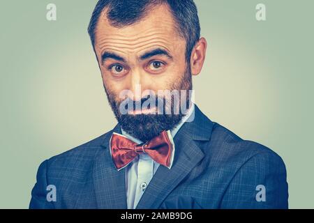 Ritratto di closeup di uomo dubbio, sospetto in abito scuro, camicia bianca, arco rosso. Barbuto uomo d'affari che guarda stupito, chiedendo alla macchina fotografica. Un singolo pers Foto Stock