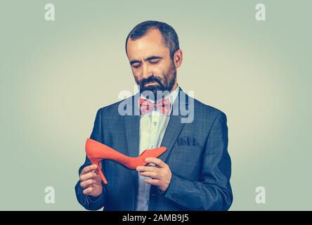Uomo pensieroso che tiene e guarda alla scarpa rossa alta-heeled. Concetto di designer di scarpe. Corpo a mezza lunghezza. Una sola persona. Verde brillante giallo gr Foto Stock