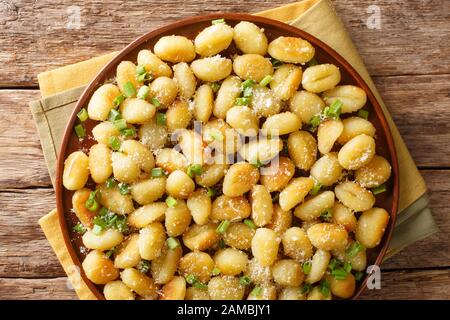 gnocchi di patate fritte a olio con aglio, formaggio e cipolle verdi si chiudono su un piatto del tavolo. Vista dall'alto orizzontale Foto Stock