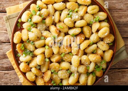 Gnocchi vegetariani di patate fritte con aglio, formaggio e cipolle verdi si chiudono su un piatto sul tavolo. Vista dall'alto orizzontale Foto Stock