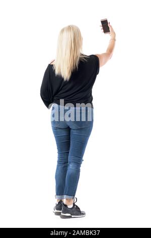 Elegante donna di mezza età vestita casual con capelli biondi in jeans che prendono selfie dall'alto. Corpo intero isolato su sfondo bianco. Foto Stock