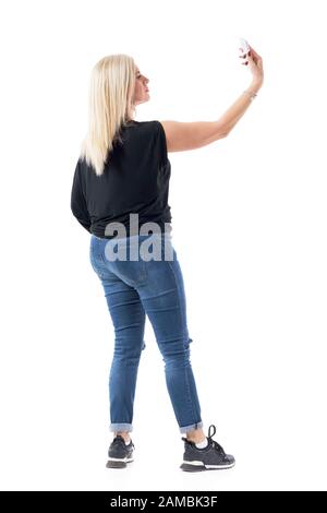 Vista laterale posteriore della moderna casual attraente bionda di mezza età donna scattare selfie foto. Corpo intero isolato su sfondo bianco. Foto Stock