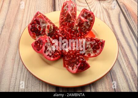 Mature succosa melagrana tagliata in più pezzi su una piastra di ceramica su uno sfondo di legno. Close up Foto Stock