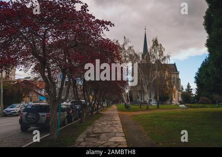 BARILOCHE, ARGENTINA, 18 GIUGNO 2019: Vista prospettica del colorato sentiero con alberi rossi accanto alla Cattedrale Nuestra Senora del Nahuel Huapi. Foto Stock