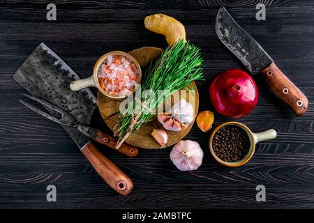 Vista dall'alto del coltello rustico a base di carne macellaio, sfaldatrice e forchetta con erbe e spezie su tavola di legno Foto Stock
